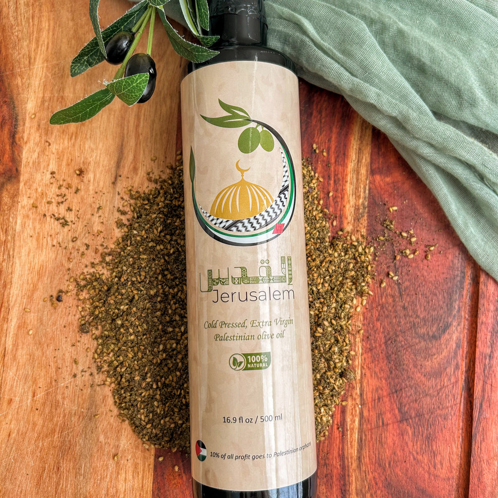 A bottle of Jerusalem olive oil with a beige label and black cap, styled on a wooden surface with scattered olive leaves and a green cloth.