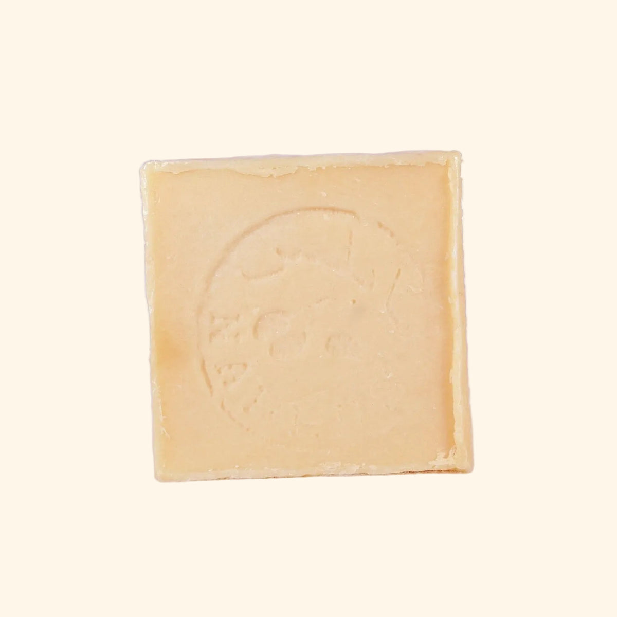 A square bar of Nabulsi olive oil soap with an embossed circular logo, standing upright on a light off-white background.